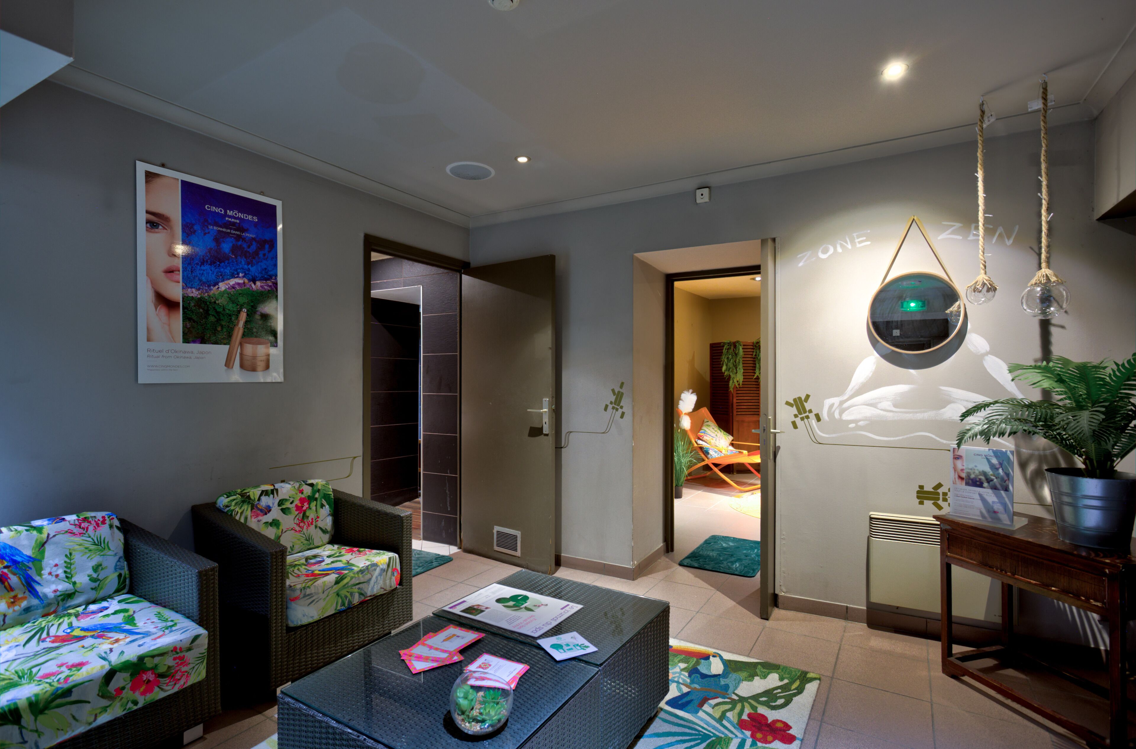 A modern living room with wicker furniture, a coffee table with papers, a poster on the wall, and a hanging light fixture.