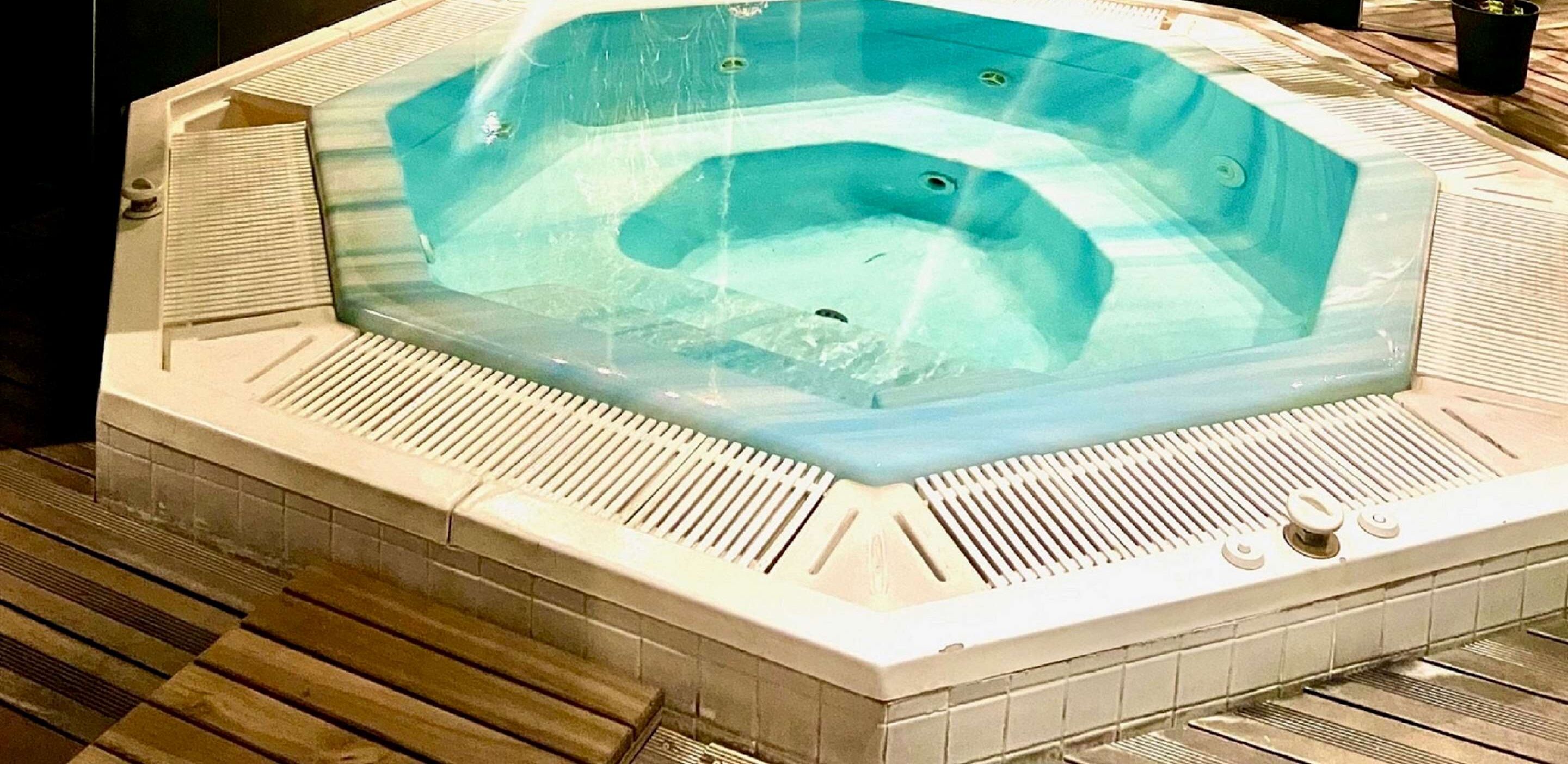 Un jacuzzi de forma rectangular, rodeado por un suelo de baldosas con un borde de madera.