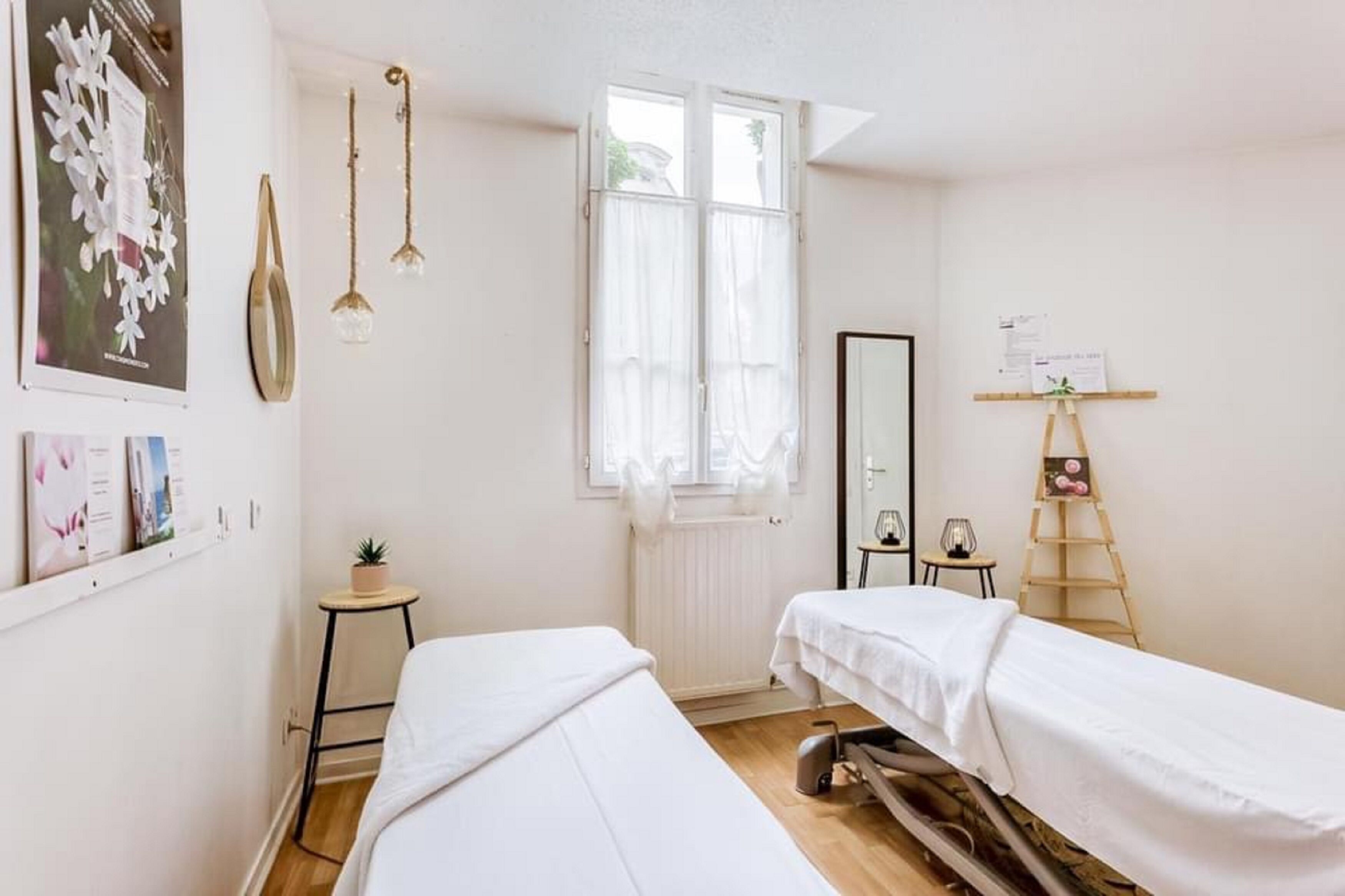 Ein Zimmer mit zwei Betten, einem Fenster mit durchsichtigen Vorhängen, einem kleinen Tisch mit Pflanze und einem Spiegel an der Wand.