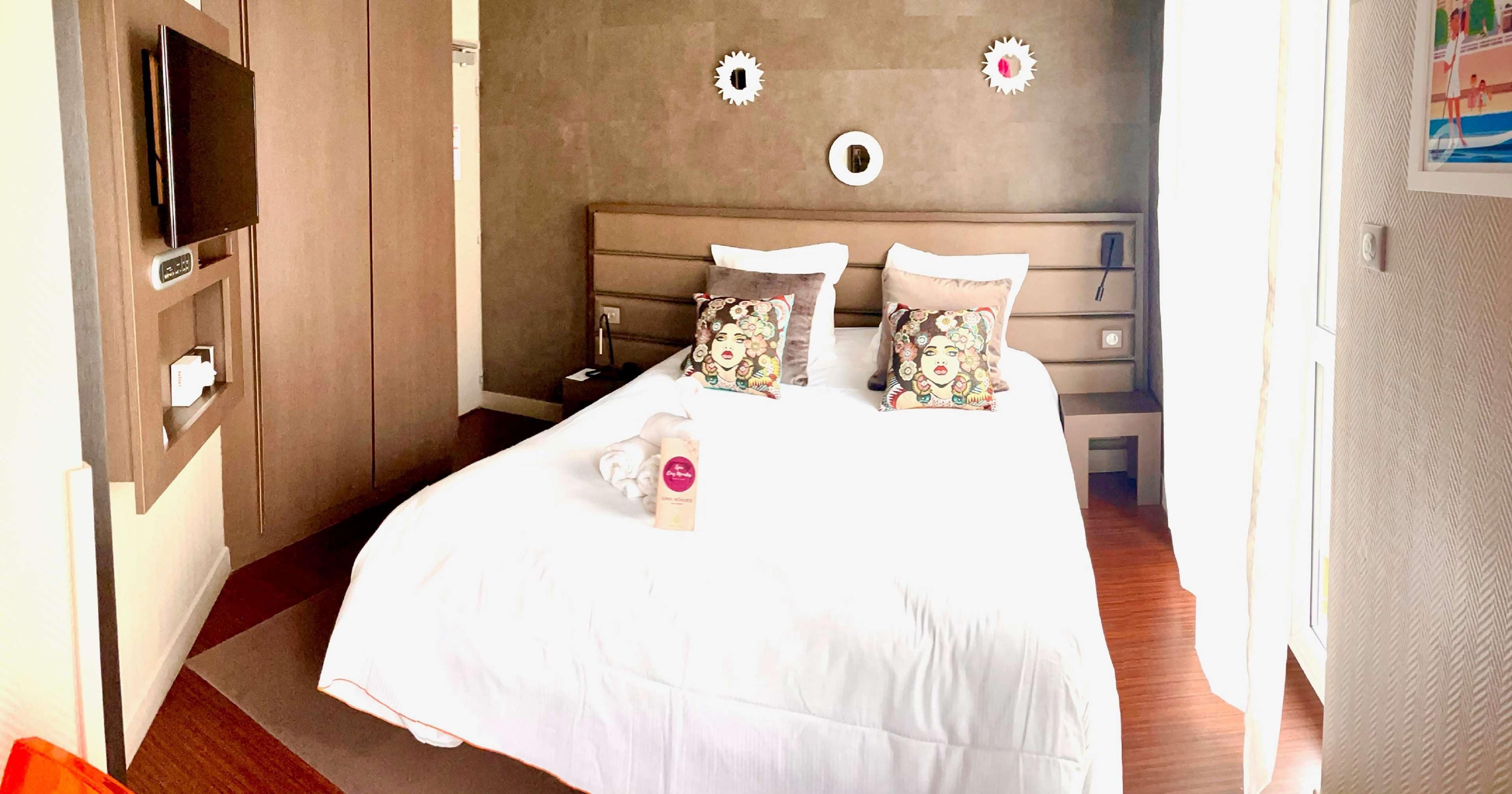A hotel room with a bed, a TV, a desk, and a wall with decorative elements.