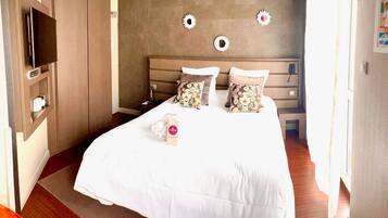 A hotel room with a bed, a TV, a desk, and a wall with decorative elements.