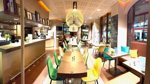 A restaurant with a long communal table, green and yellow chairs, and a hanging light fixture. - Hotel Kyriad Vichy Spa Cinq Mondes (Vichy)