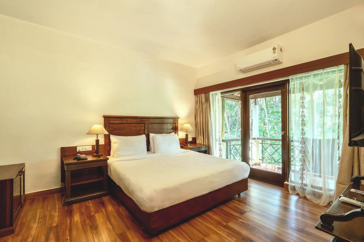 A hotel room with a wooden bed, two bedside tables with lamps, a TV, and a balcony with curtains.