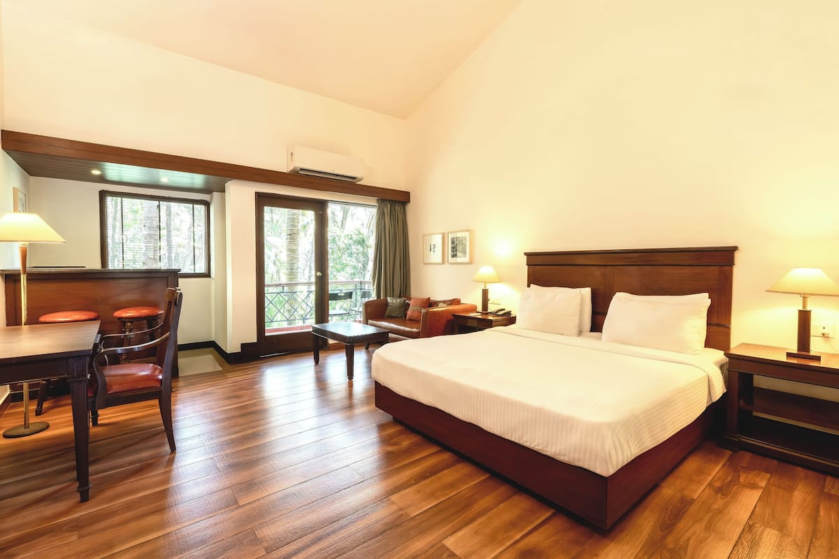 A hotel room with a large bed, wooden flooring, a desk with a chair, a small table, and a sofa.