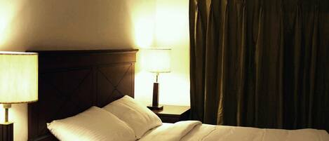 A hotel room with a bed, two bedside lamps, and a curtain.