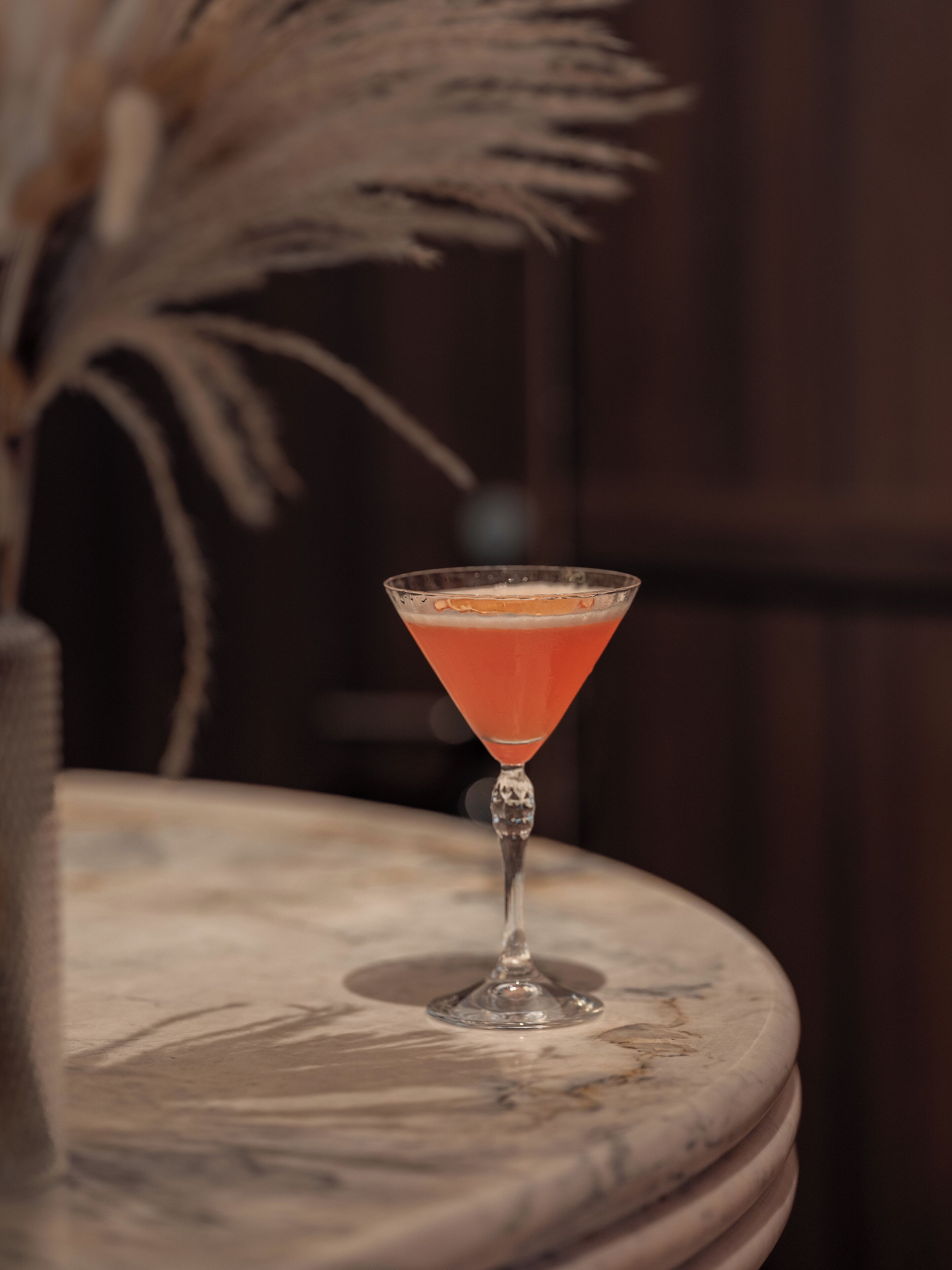 A martini glass with a clear stem and a decorative pattern on the base, placed on a marble surface.