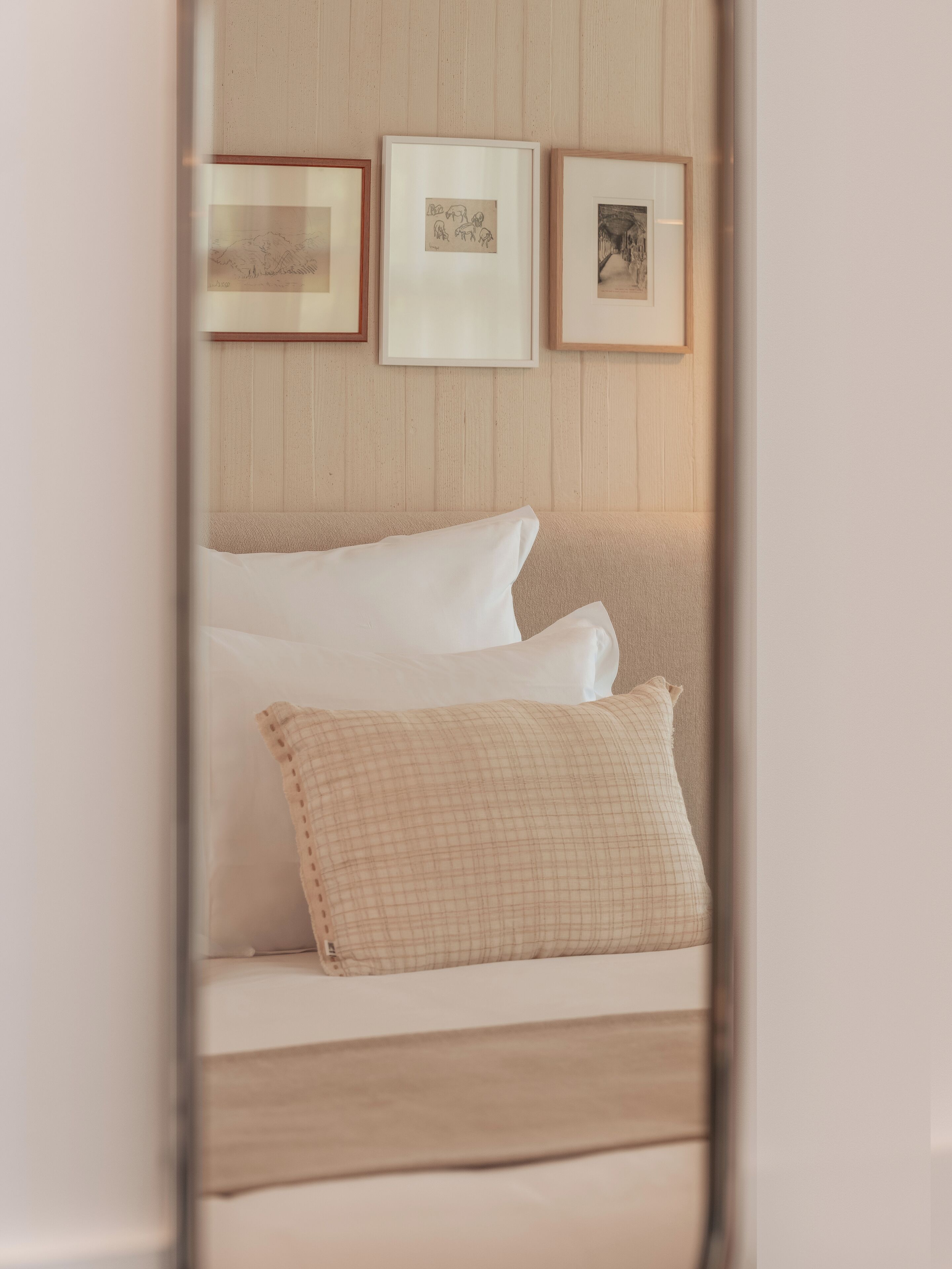 A bedroom with a bed, pillows, and three framed pictures on the wall.