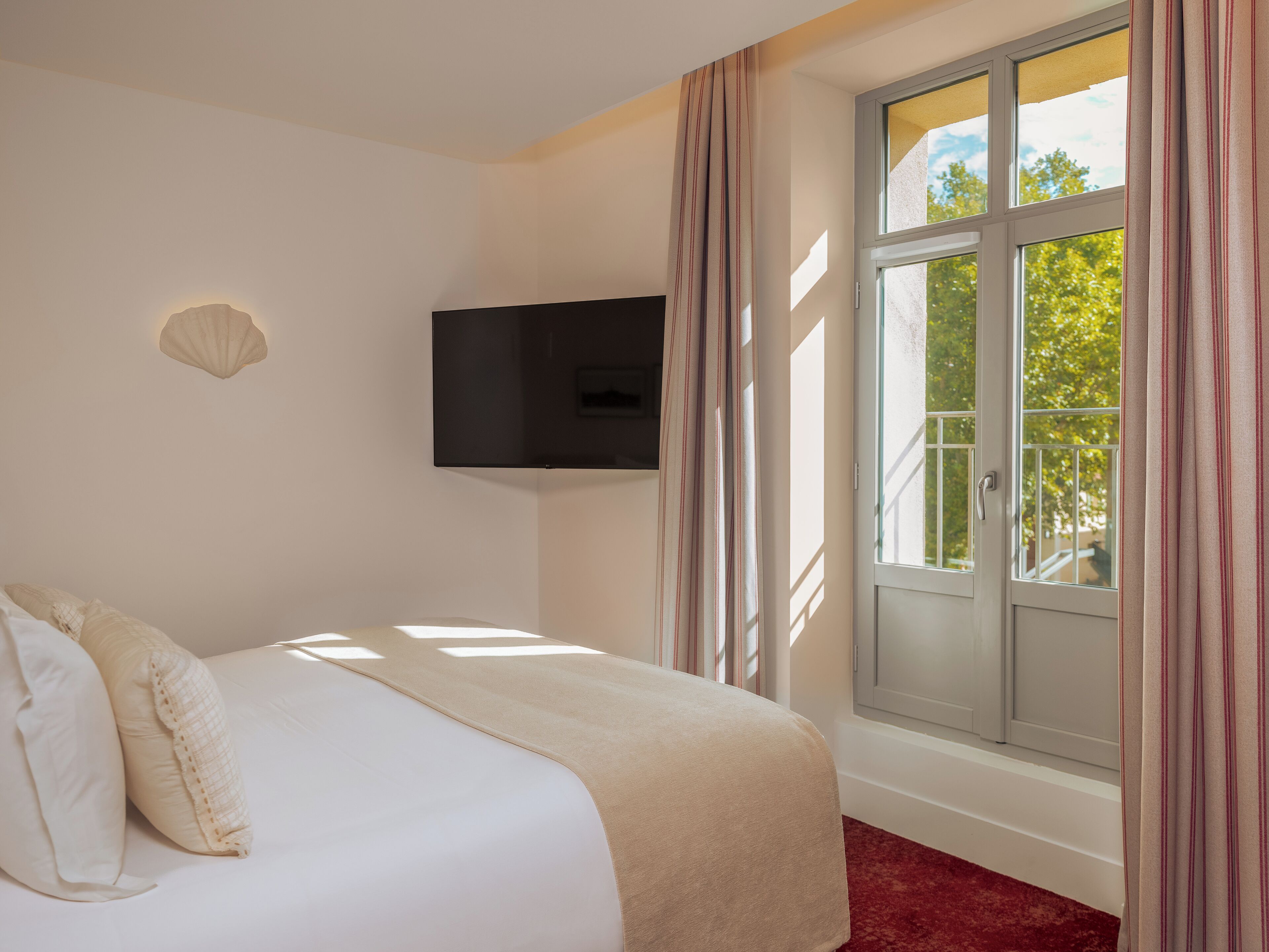 A hotel room with a bed, a television mounted on the wall, and a window with curtains.