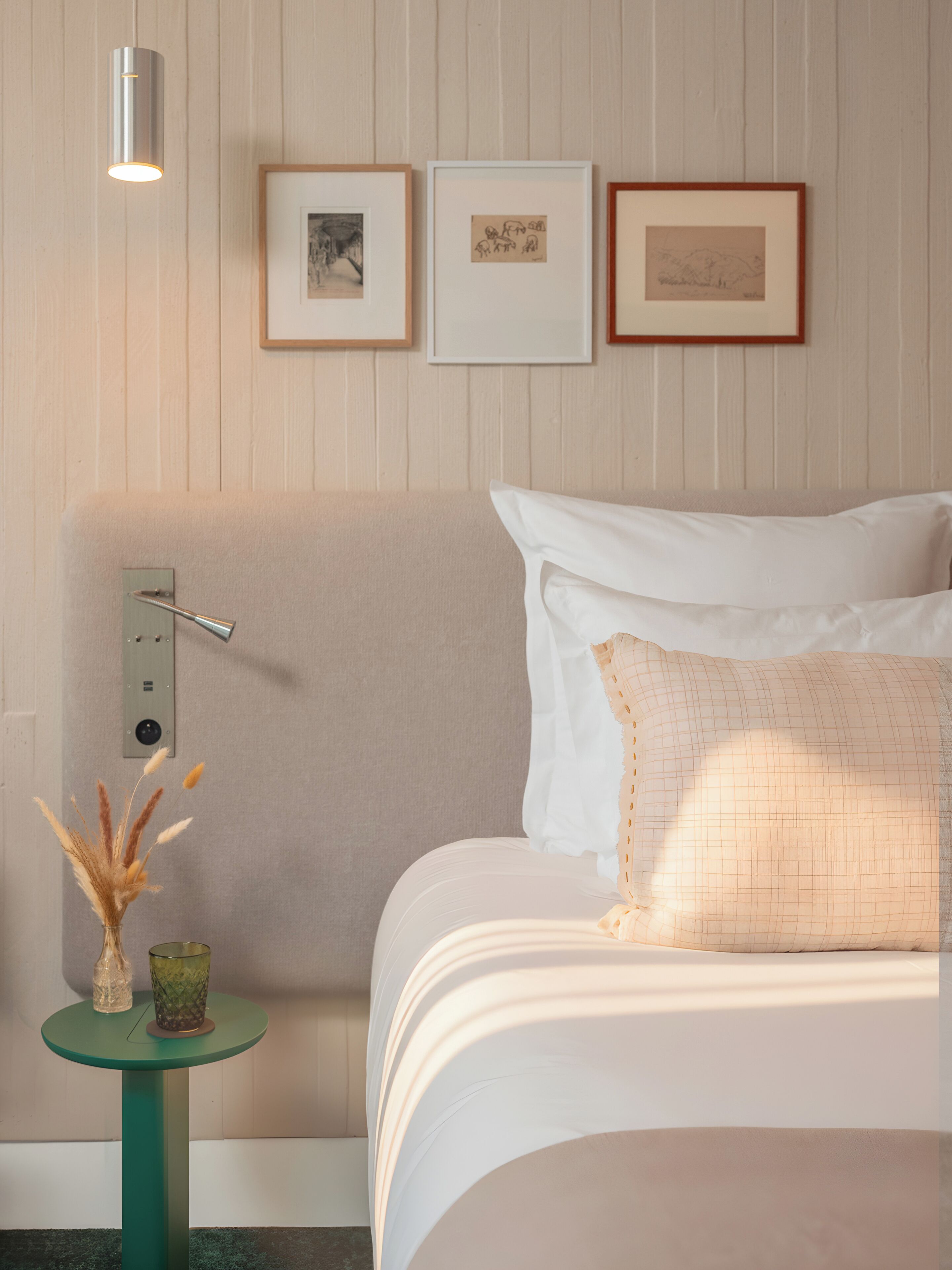 A hotel room with a bed, a bedside table with a lamp, and framed pictures on the wall.