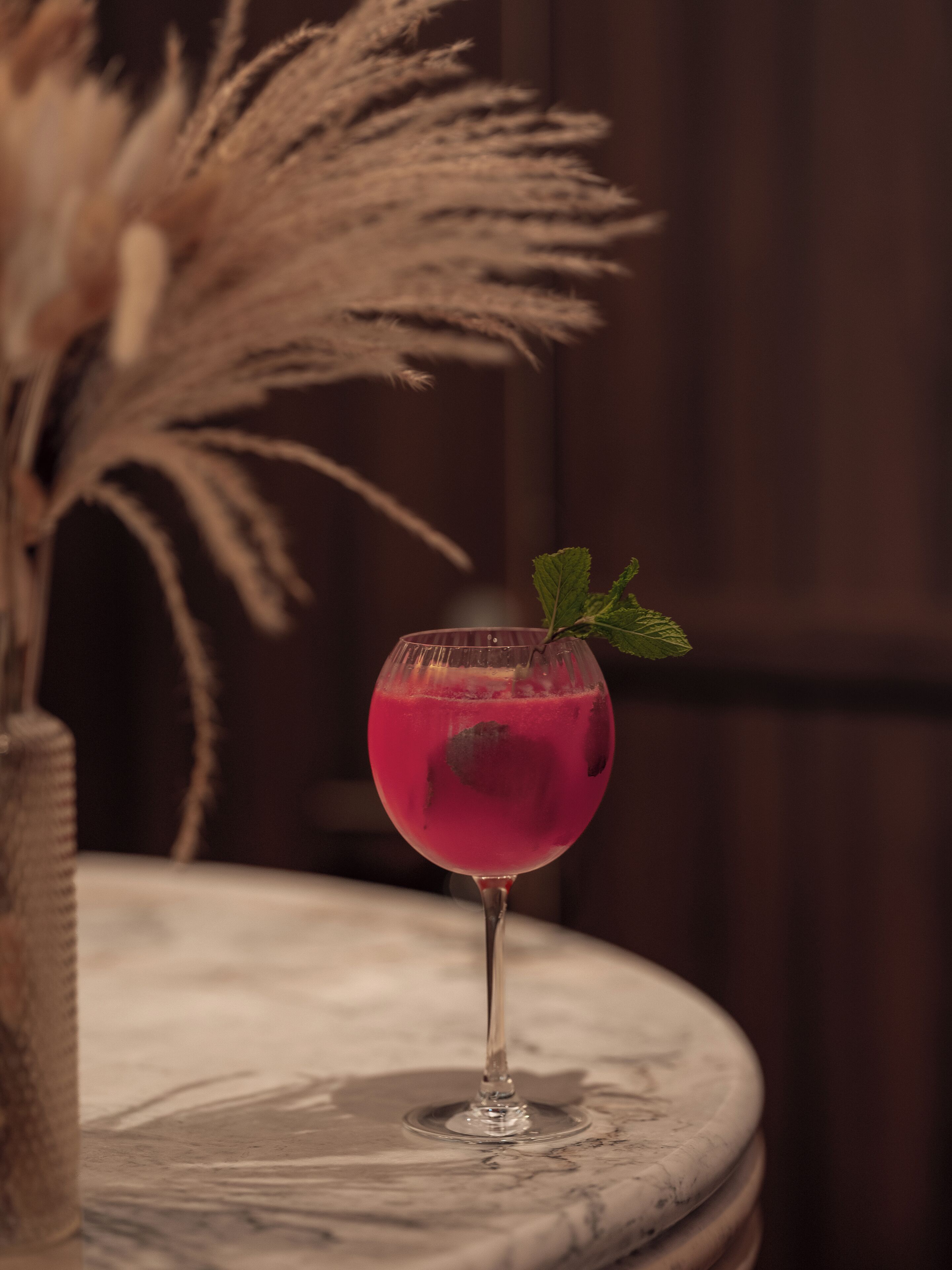 A glass of pink drink on a marble table with pampas grass in the background.