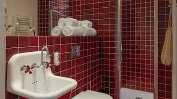 Casa de banho com parede revestida a azulejos vermelhos, lavatório branco com puxadores vermelhos, sanita branca e área de duche.