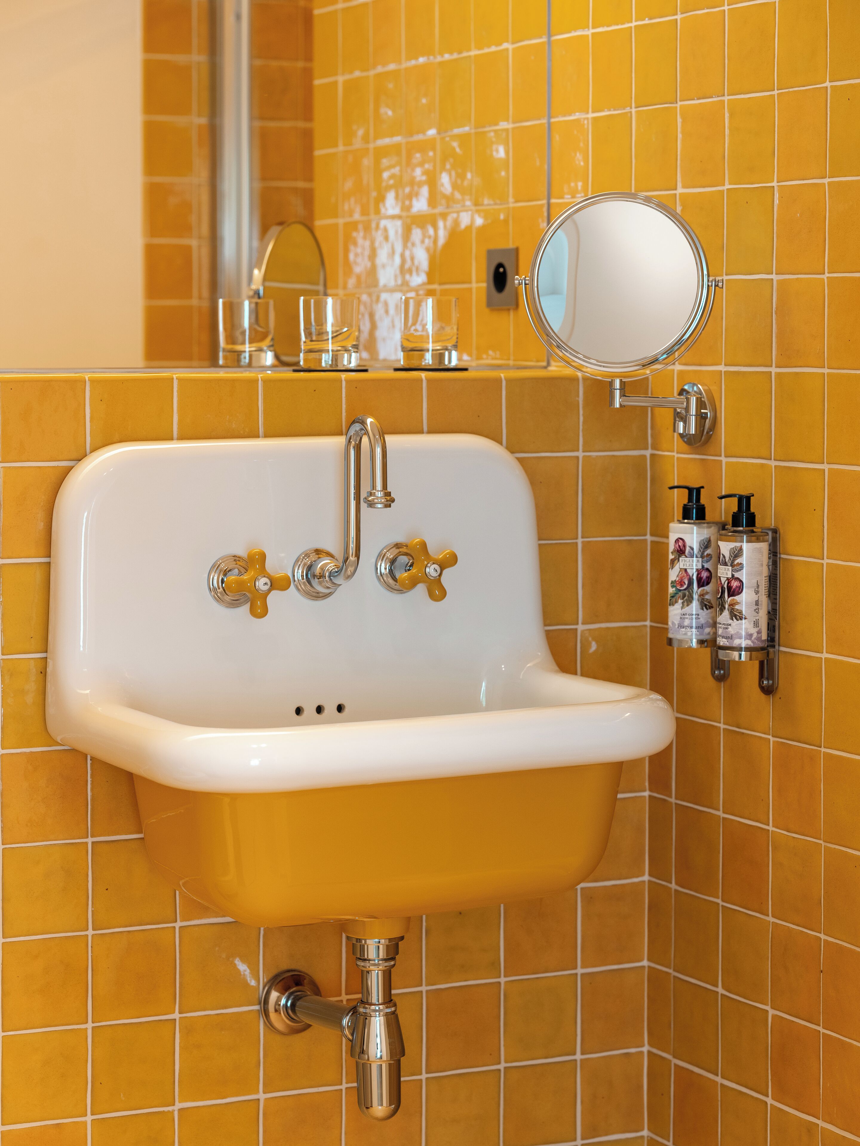 A bathroom with a white sink, yellow tiled walls, a mirror, and two hand soap dispensers.