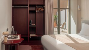 Habitación de hotel con cama, escritorio con silla, armario y puerta corrediza de vidrio a un balcón.