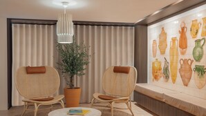 Una habitación con dos sillones de mimbre, una mesa redonda con libros, una planta en maceta y una pared con jarrones de cerámica.