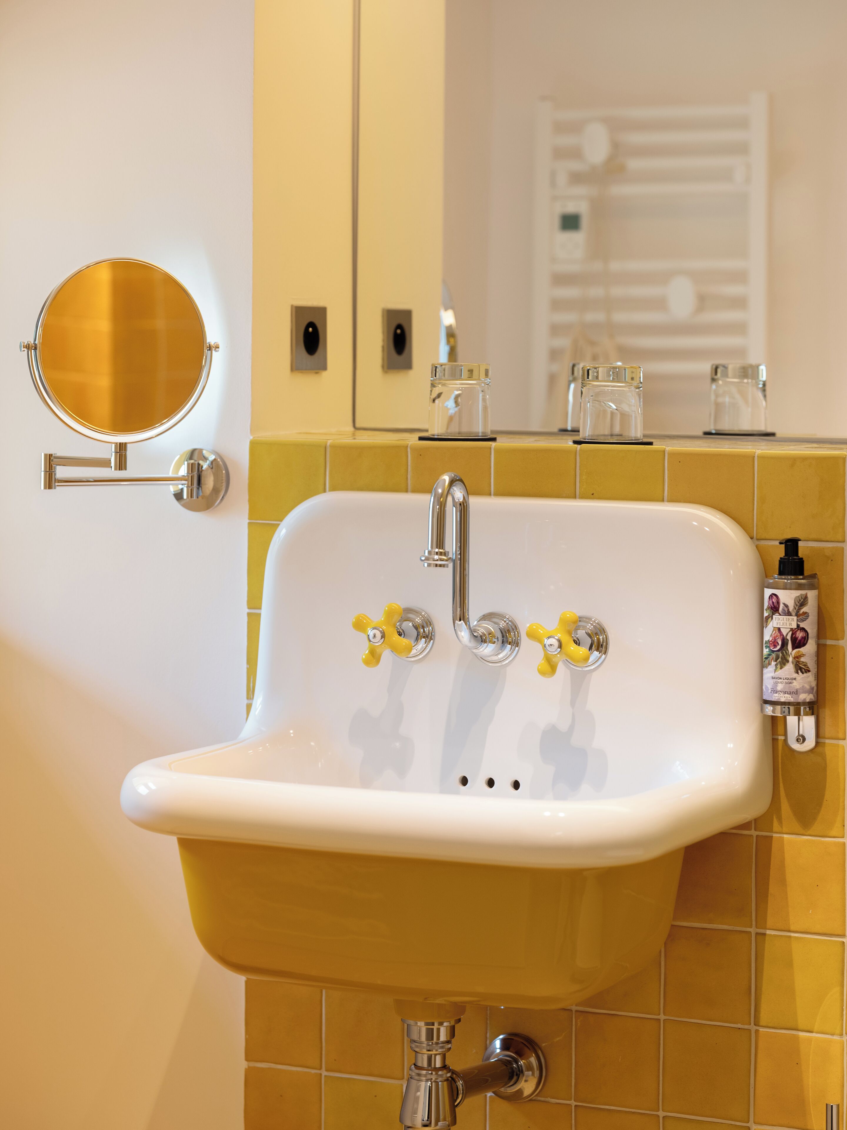 Un baño con un lavamanos blanco, azulejos amarillos, un espejo redondo y un dispensador de jabón.