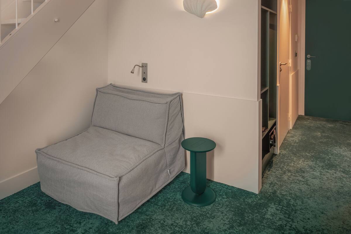 A staircase with white railings, a grey sofa, a small green side table, and a wall-mounted light fixture.