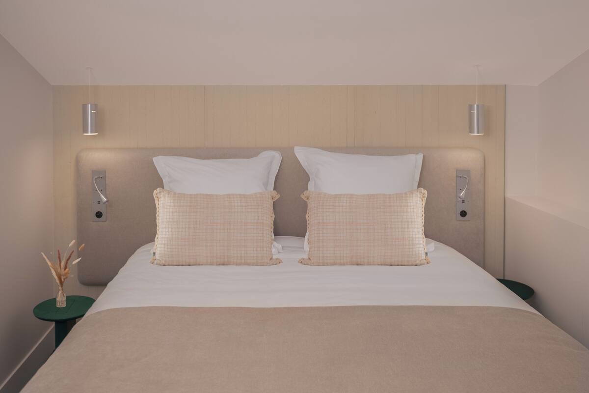 A modern hotel room with a large bed, two bedside tables, and a wall-mounted light fixture.