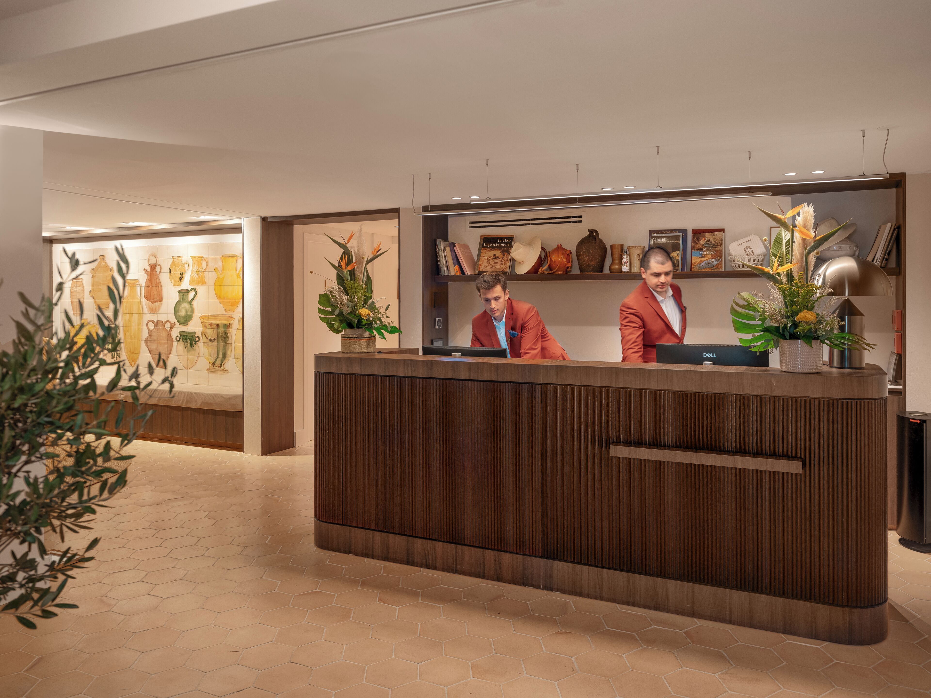 A reception desk with two individuals behind it, a display of vases, and a plant on the counter.