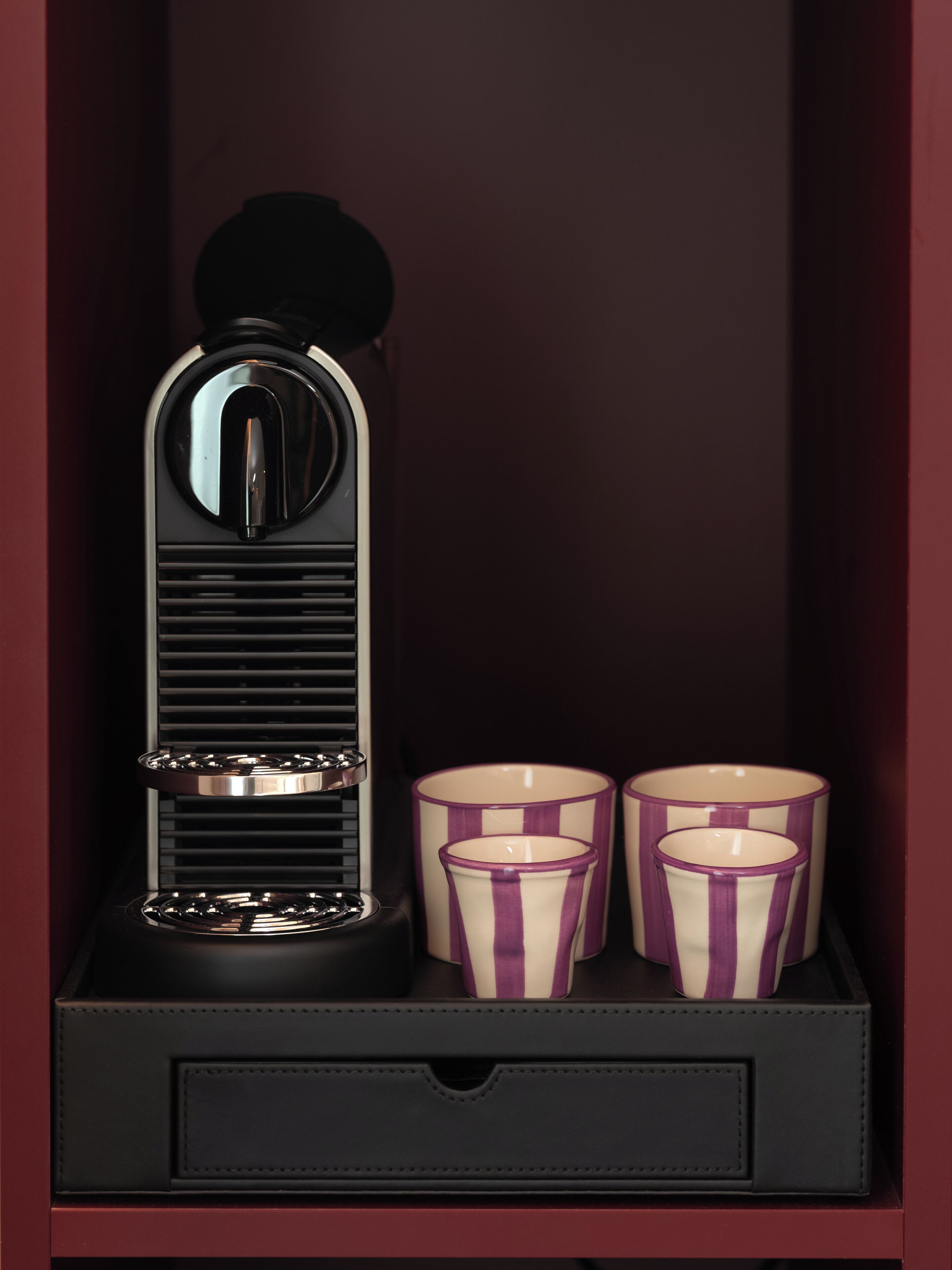A black espresso machine with two purple-striped cups in a drawer.