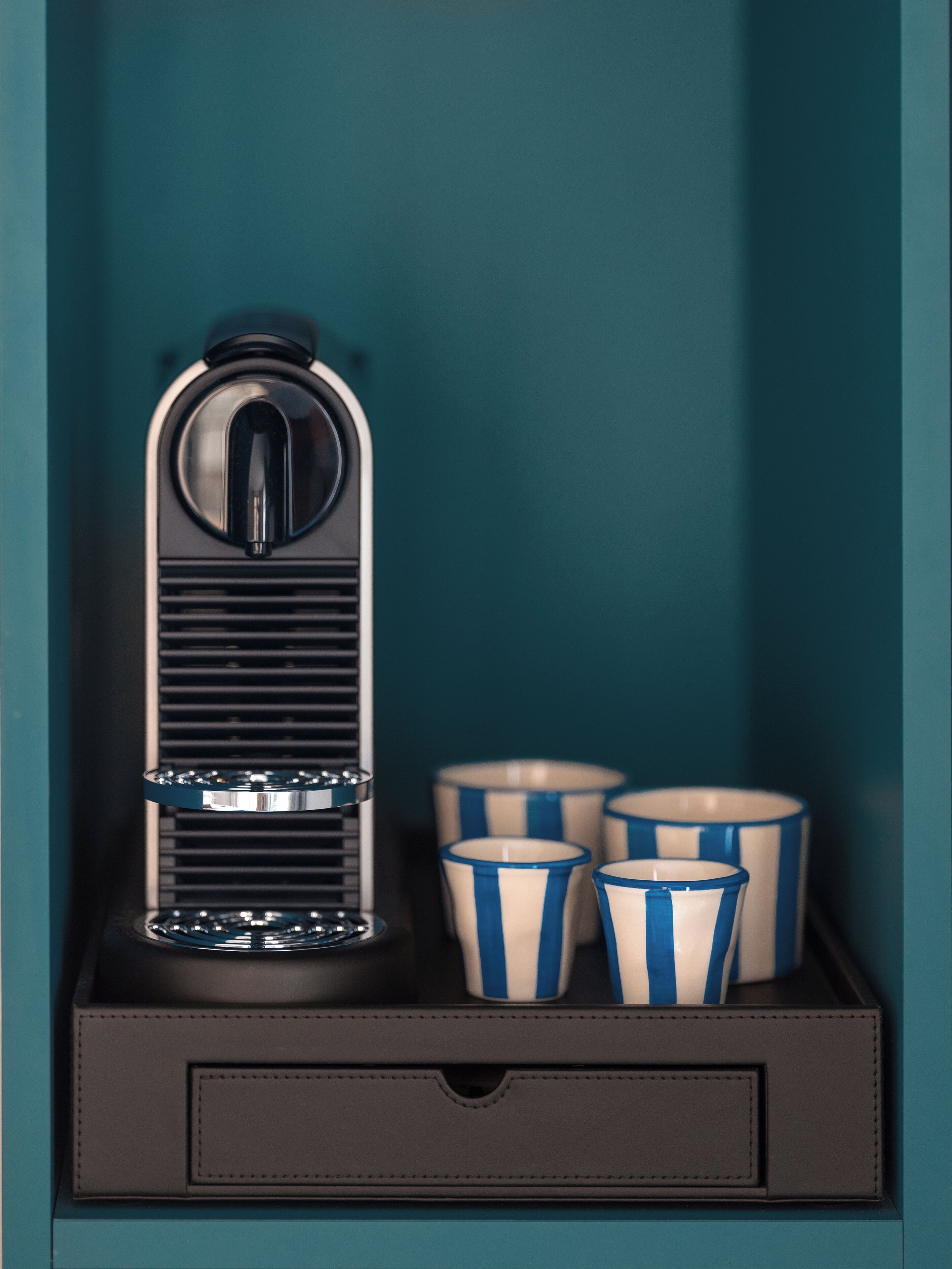 A coffee machine in a drawer with four striped cups.