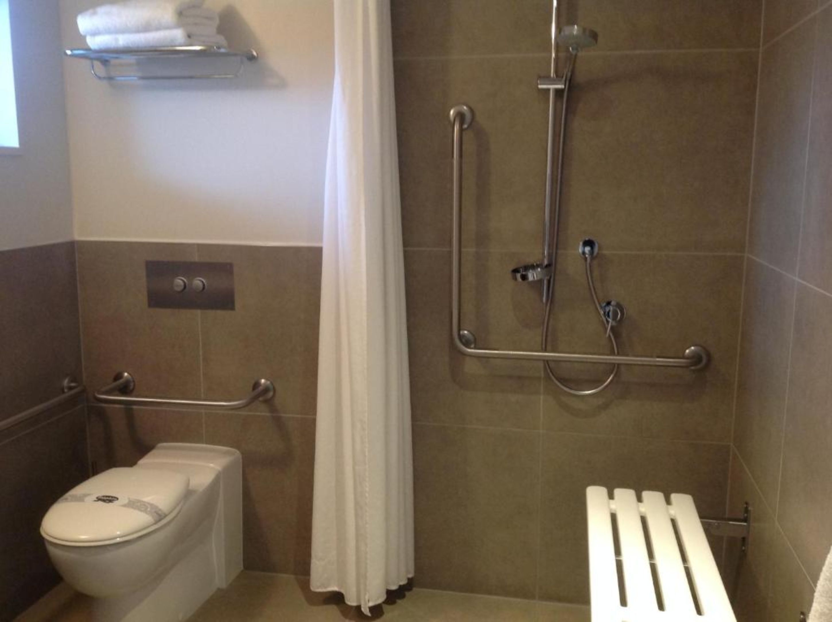 A bathroom with a toilet, a shower with grab bars, and a towel rack.