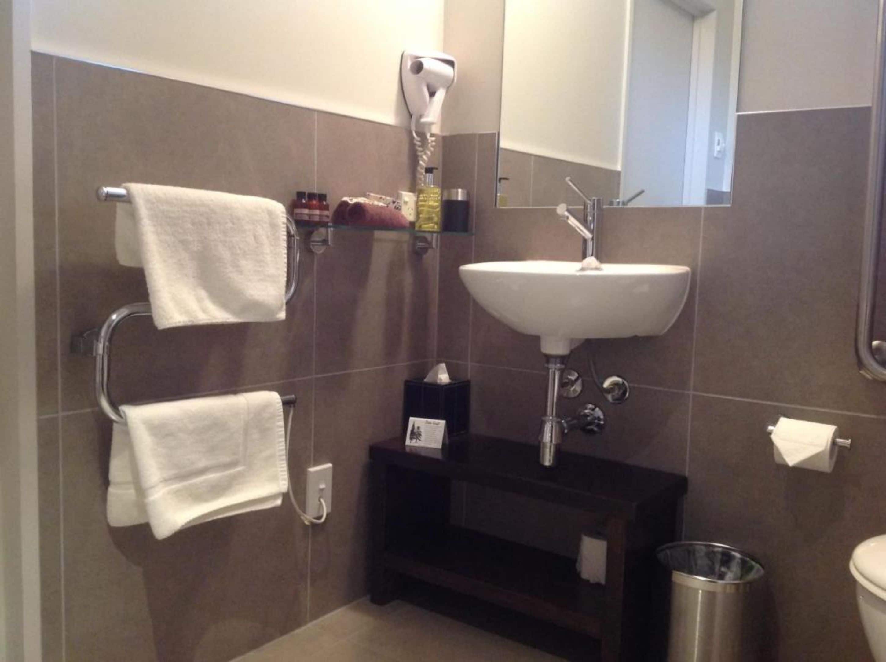 A bathroom with a white sink, a towel rack, a hairdryer, and a trash can.
