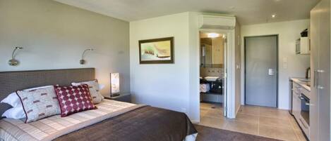 A bedroom with a large bed, a nightstand, a wall-mounted lamp, and a door leading to a bathroom.