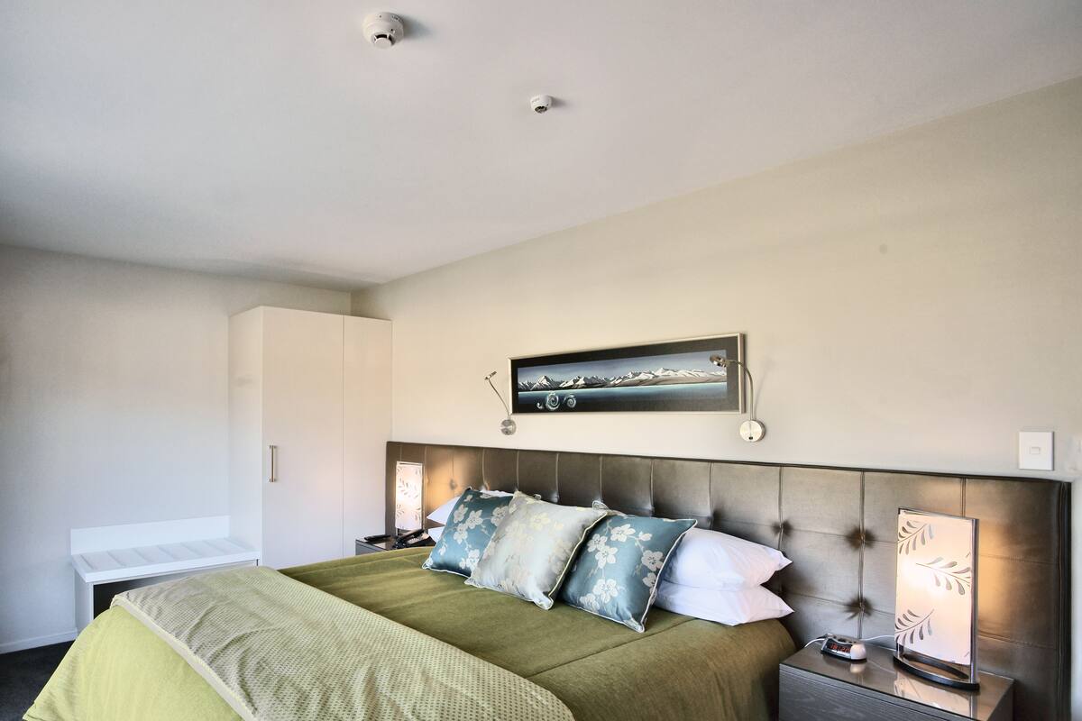 A neatly arranged bedroom with a bed, bedside tables, a nightstand, a lamp, and a wall-mounted picture.