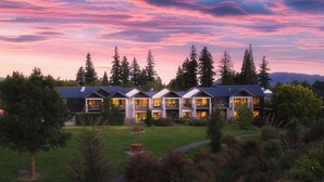 A multi-story hotel with balconies, a well-maintained lawn, and a view of the surrounding forest.