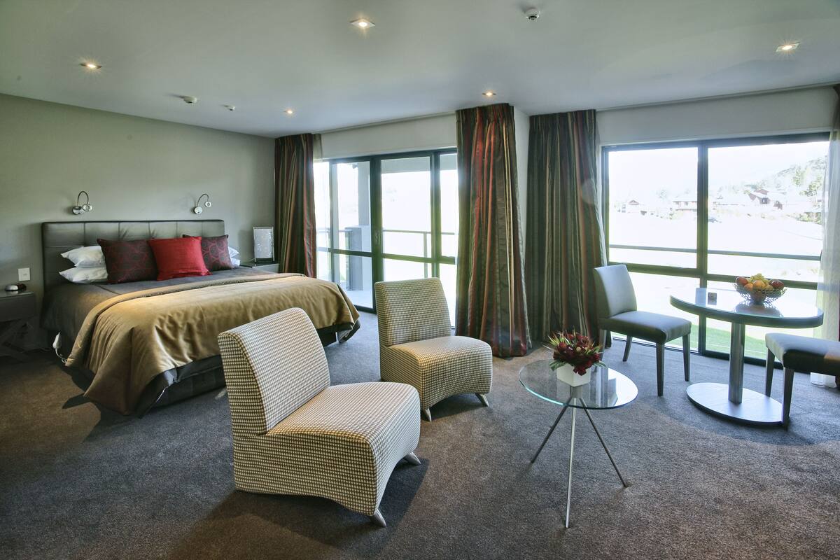 A hotel room with a bed, two armchairs, a small table, and a large window with curtains.