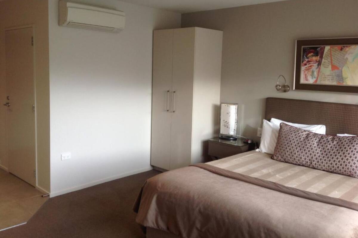 A bedroom with a bed, a wardrobe, a bedside table, and an air conditioning unit.
