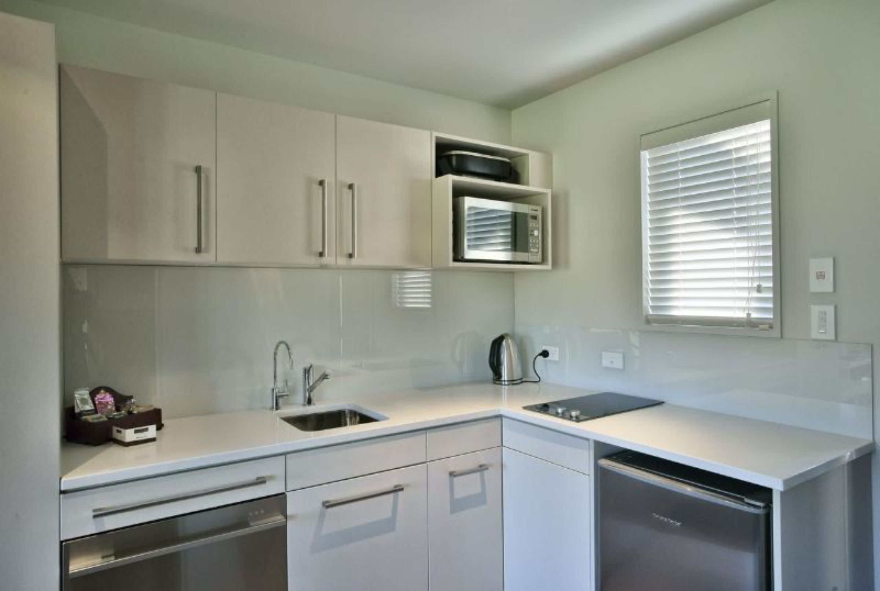 Una cocina moderna con armarios blancos, microondas integrado, hervidor y lavavajillas.
