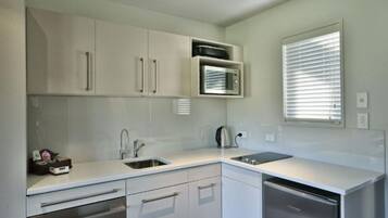 Una cocina moderna con armarios blancos, microondas integrado, hervidor y lavavajillas.