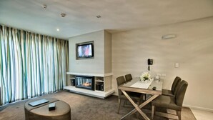 A modern living room with a fireplace, a dining table with chairs, a TV mounted on the wall, and a striped curtain.