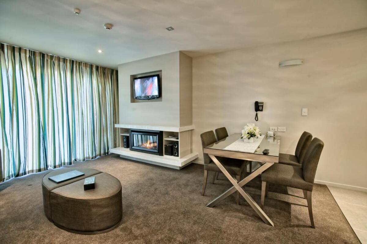 A modern living room with a fireplace, a dining table with chairs, a TV mounted on the wall, and a striped curtain.