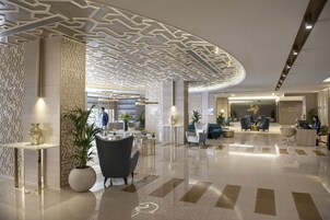 A modern lobby with a geometric ceiling design, a reception desk, seating area, and a cafe.