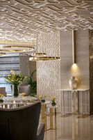 A modern interior with a geometric patterned wall, a round dining table with chairs, and a vase with yellow flowers.