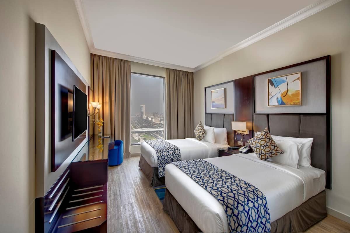 A hotel room with two beds, a TV, a desk, and a city view.