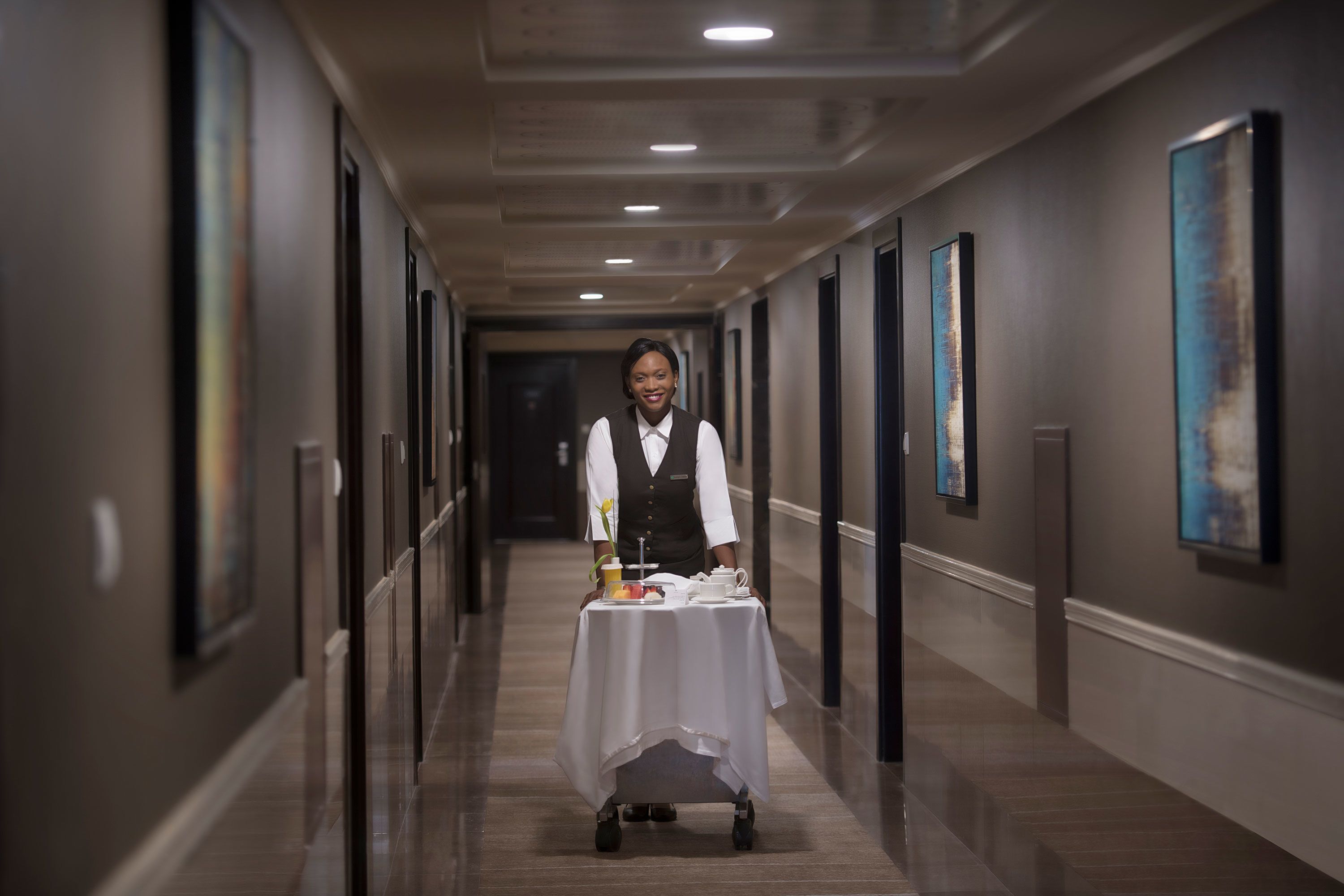 A hotel corridor with a service cart, framed artwork on the walls, and a polished floor.
