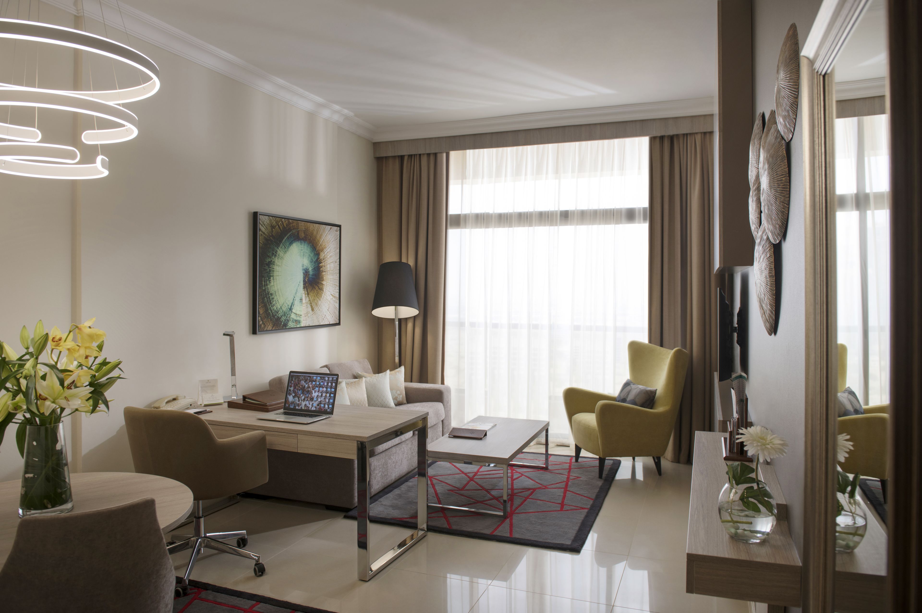 Una habitación de hotel moderna con sofá, sillones, una mesita de centro, un escritorio y un ventanal con cortinas.