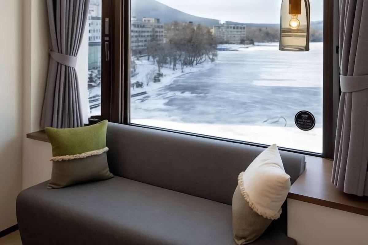 A room with a sofa, a window with curtains, and a view of a snowy landscape.