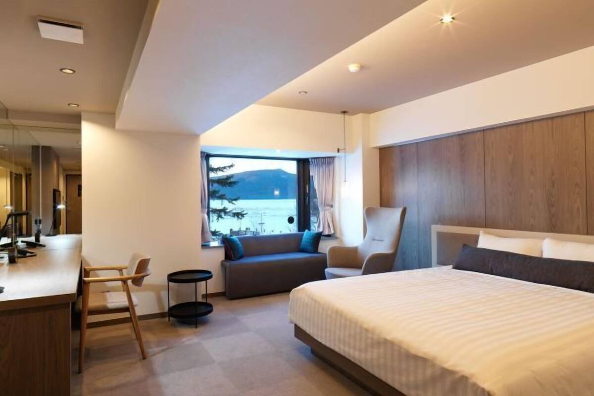 A modern hotel room with a large bed, a seating area with a view, and a desk with a chair.