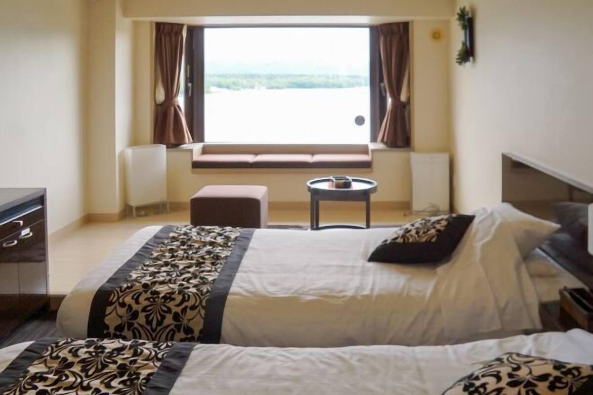 A hotel room with two beds, a small table, a sofa, and a window with curtains.