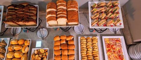 Un bufé con diferentes opciones de comida, como sándwiches, pasteles y pizza.