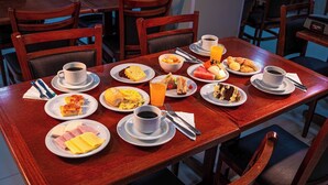 Una mesa de comedor con platos de comida, tazas de café y un vaso de jugo.
