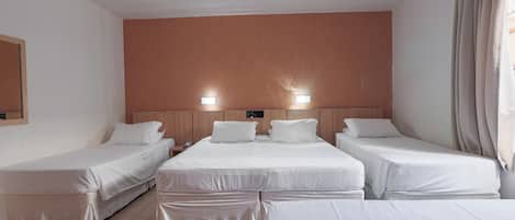 Habitación de hotel con tres camas individuales, un cabecero de madera, una mesita de noche pequeña con una lámpara y un espejo grande en la pared.