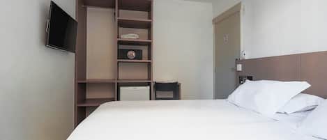 Una habitación de hotel con cama, televisor montado en la pared, armario con estantes múltiples y puerta con letrero de 'No pasar'.