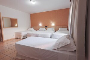Habitación de hotel con tres camas, un espejo grande y un cabecero de madera.