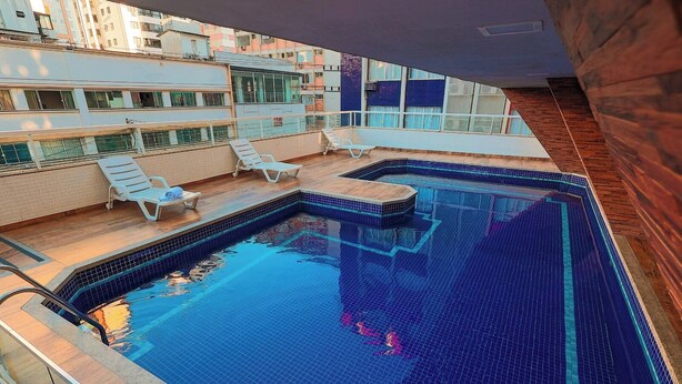 Una piscina con solárium empedrado, sillones de descanso y vistas a edificios circundantes.