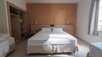 A hotel room with a large bed, a wardrobe, a bedside table with a phone, and a window with curtains.